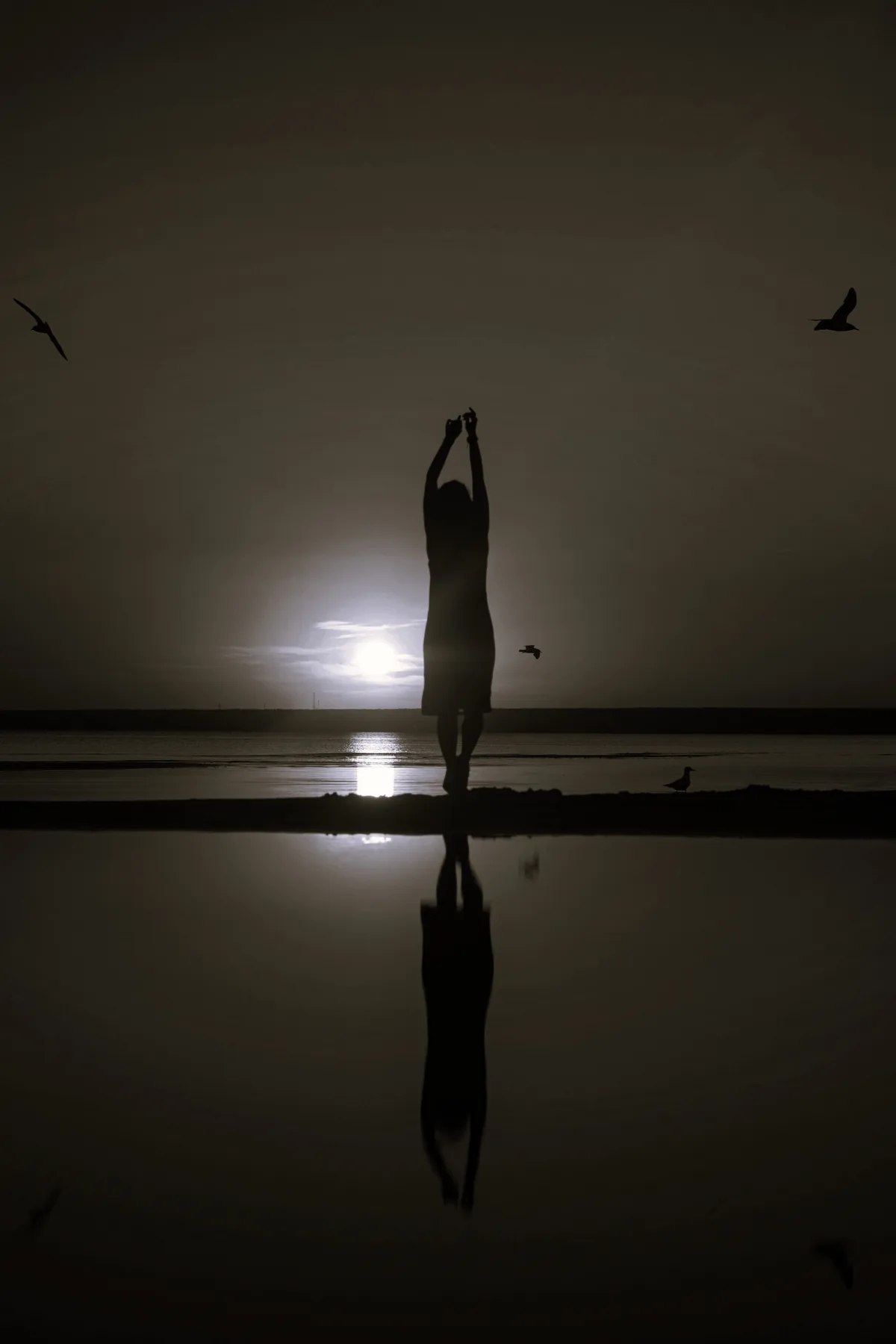 Woman meditating, facing the sea at dusk.