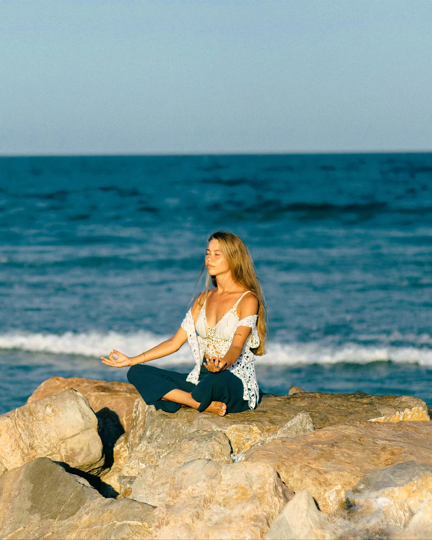 Woman in lotus on rocks by the clear Aegean.